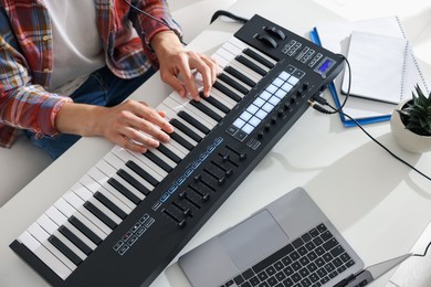 Photo of Man working with MIDI keyboard at white table indoors,