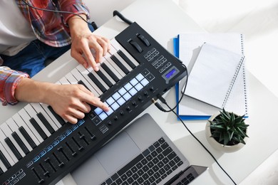 Photo of Man working with MIDI keyboard at white table indoors, above view