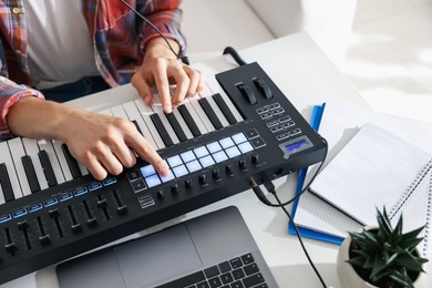 Photo of Man working with MIDI keyboard at white table indoors, above view