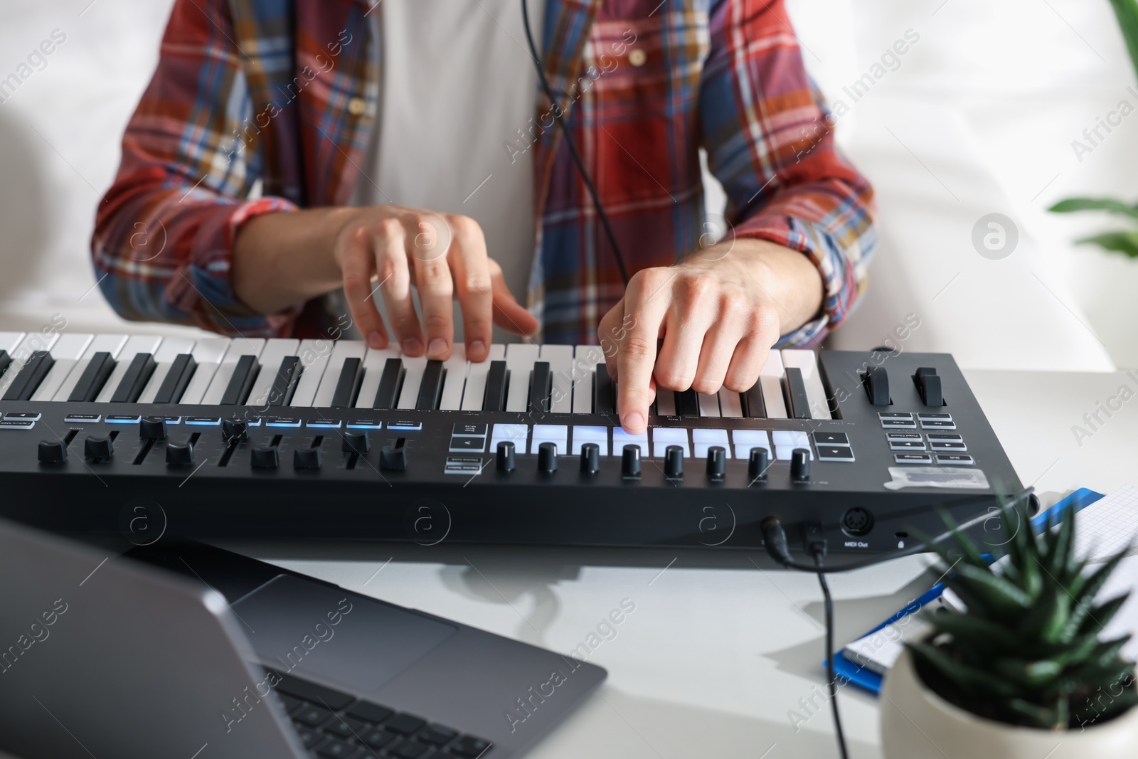Photo of Man working with MIDI keyboard at white table indoors, closeup