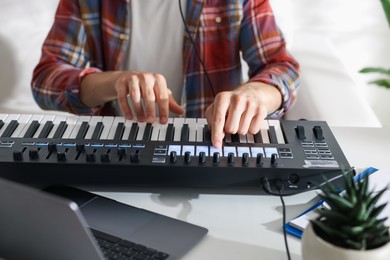 Photo of Man working with MIDI keyboard at white table indoors, closeup
