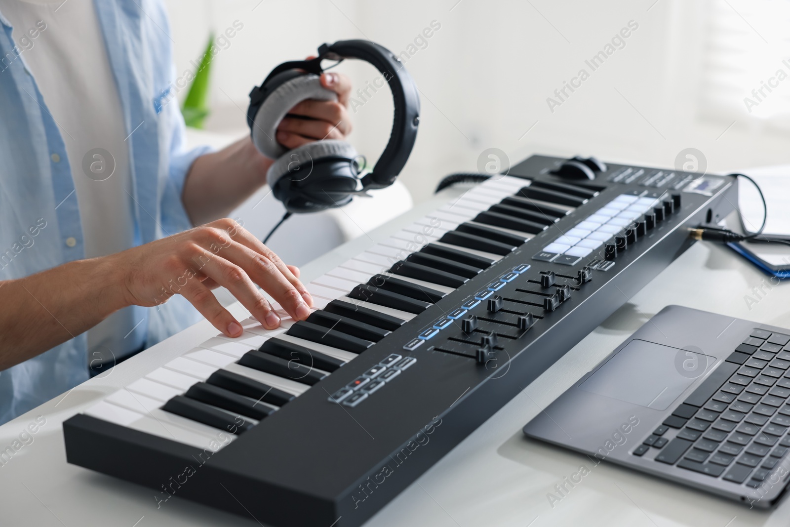 Photo of Man with headphones working with MIDI keyboard at white table indoors, closeup