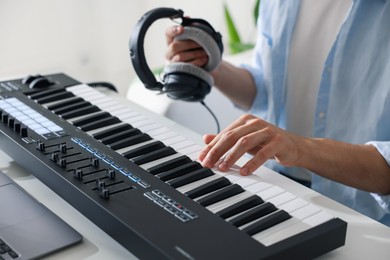 Photo of Man working with MIDI keyboard at table indoors, closeup