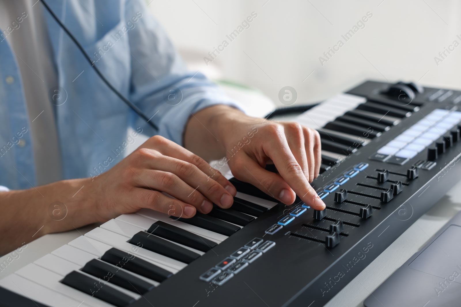 Photo of Man working with MIDI keyboard at table indoors, closeup