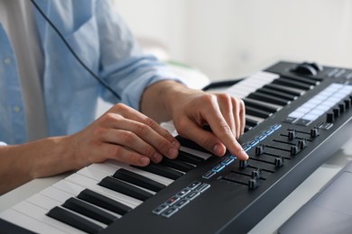 Photo of Man working with MIDI keyboard at table indoors, closeup