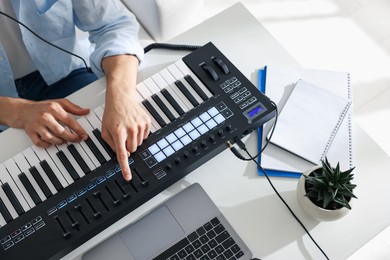 Photo of Man working with MIDI keyboard at white table indoors, above view