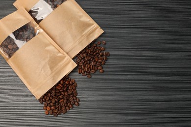 Photo of Zipper stand-up pouches and coffee beans on black textured table, flat lay. Mockup for design