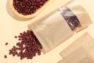 Photo of Zipper stand-up pouches and dry kidney beans on beige background, flat lay. Mockup for design
