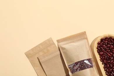 Photo of Zipper stand-up pouches and dry kidney beans on beige background, flat lay. Mockup for design