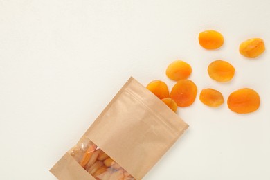 Photo of Zipper stand-up pouch with dried apricots on white table, flat lay. Mockup for design