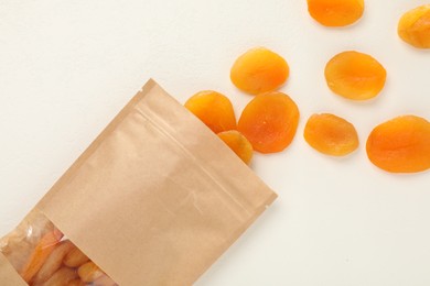 Photo of Zipper stand-up pouch with dried apricots on white table, flat lay. Mockup for design