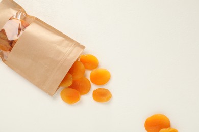 Photo of Zipper stand-up pouch with dried apricots on white table, flat lay. Mockup for design