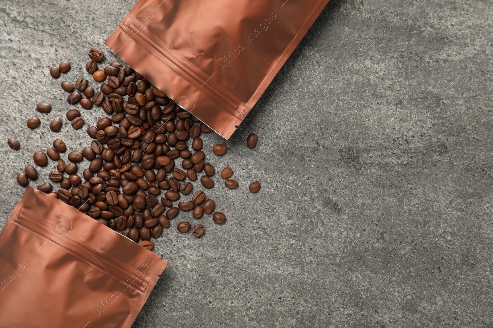 Photo of Zipper stand-up pouches and coffee beans on grey table, flat lay. Space for text