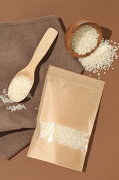 Photo of Zipper stand-up pouch and white rice on brown background, flat lay. Mockup for design