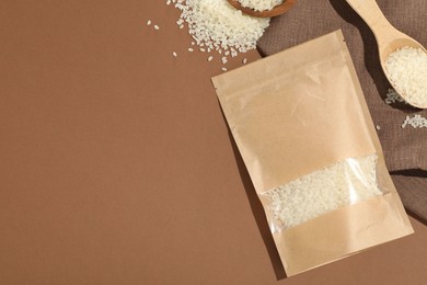 Photo of Zipper stand-up pouch and white rice on brown background, flat lay. Mockup for design