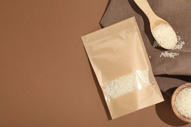 Photo of Zipper stand-up pouch and white rice on brown background, flat lay. Mockup for design
