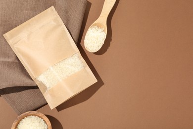 Photo of Zipper stand-up pouch and white rice on brown background, flat lay. Mockup for design