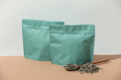Photo of Zipper stand-up pouches and dry leaves on beige table against light grey background, mockup for design