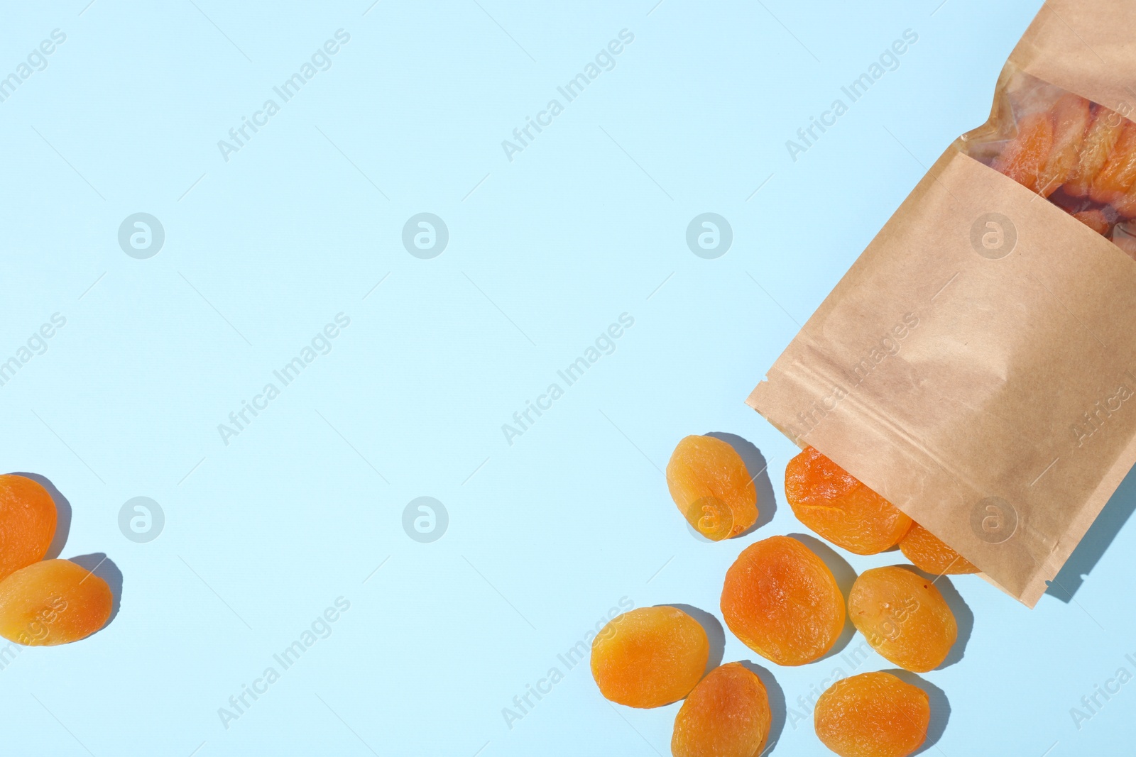 Photo of Zipper stand-up pouch with dried apricots on light blue background, flat lay. Mockup for design