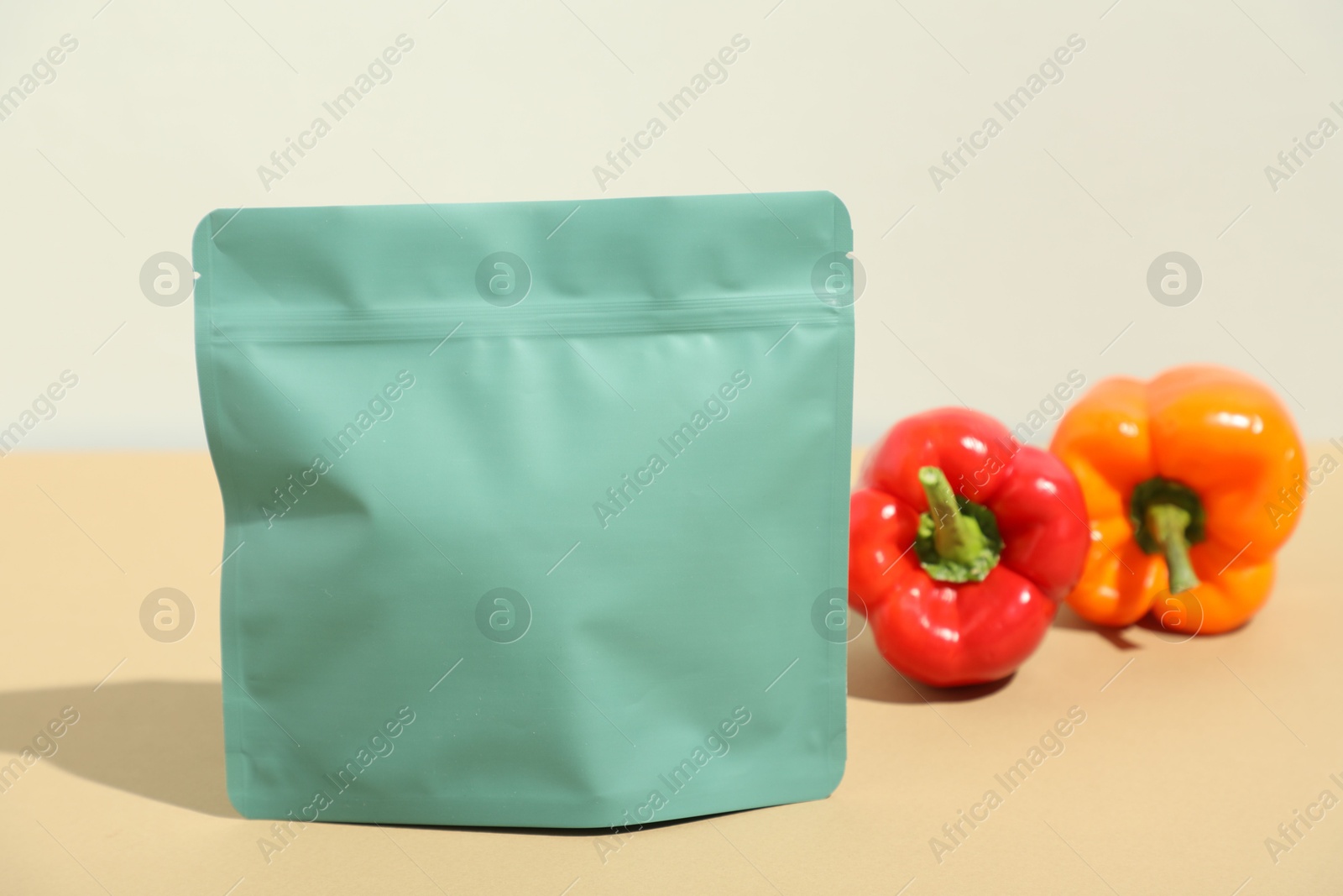 Photo of Zipper stand-up pouch and bell peppers on beige table, closeup. Mockup for design