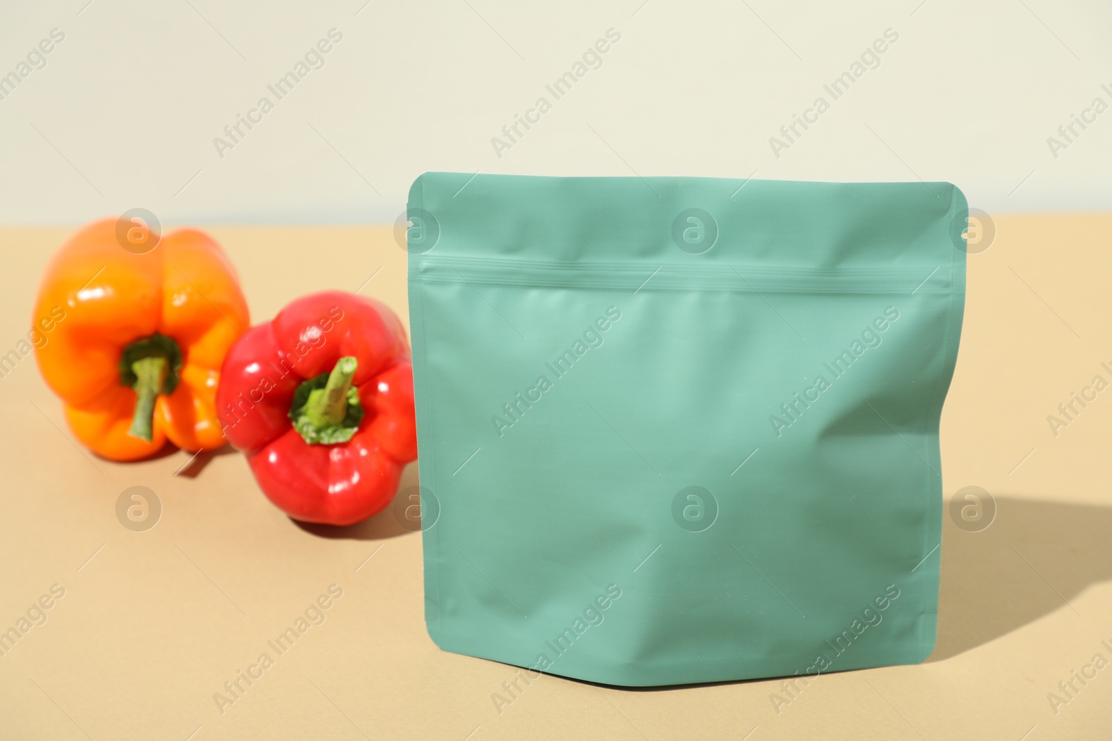 Photo of Zipper stand-up pouch and bell peppers on beige table, closeup. Mockup for design