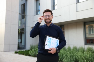 Photo of Happy businessman with clipboard near office building