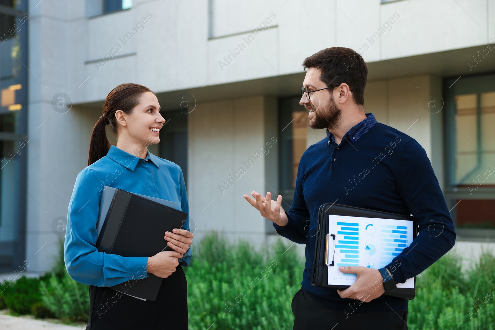Photo of Happy coworkers discussing something near office building
