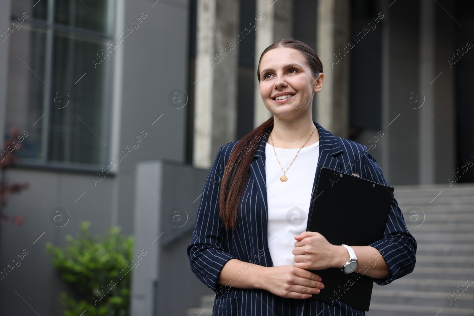 Happy businesswoman with folder near office building. Space for text Photo of Happy businesswoman with folder near office building. Space for text