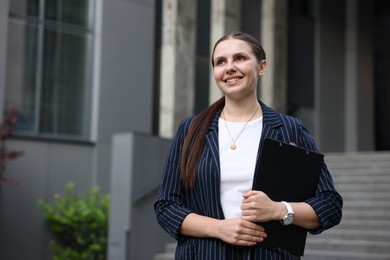 Photo of Happy businesswoman with folder near office building. Space for text
