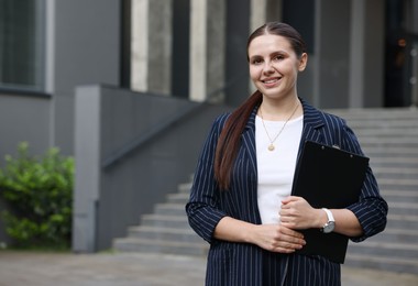 Photo of Happy businesswoman with folder near office building. Space for text