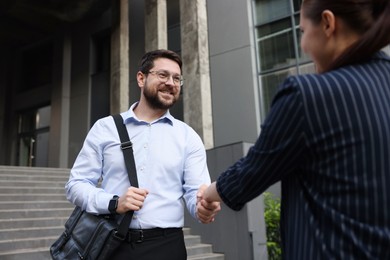 Photo of Happy coworkers shaking hands near office building