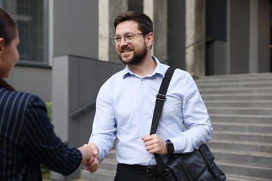 Photo of Happy coworkers shaking hands near office building