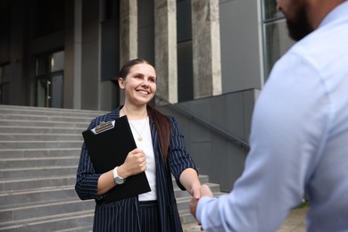 Photo of Happy coworkers shaking hands near office building