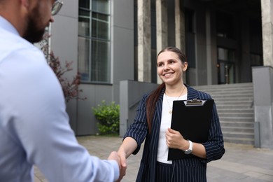 Photo of Happy coworkers shaking hands near office building