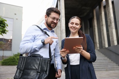 Photo of Happy coworkers with tablet near office building