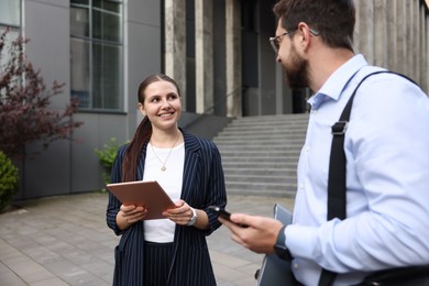 Photo of Happy coworkers with tablet and smartphone near office building