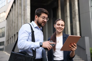 Photo of Happy coworkers with tablet and smartphone near office building