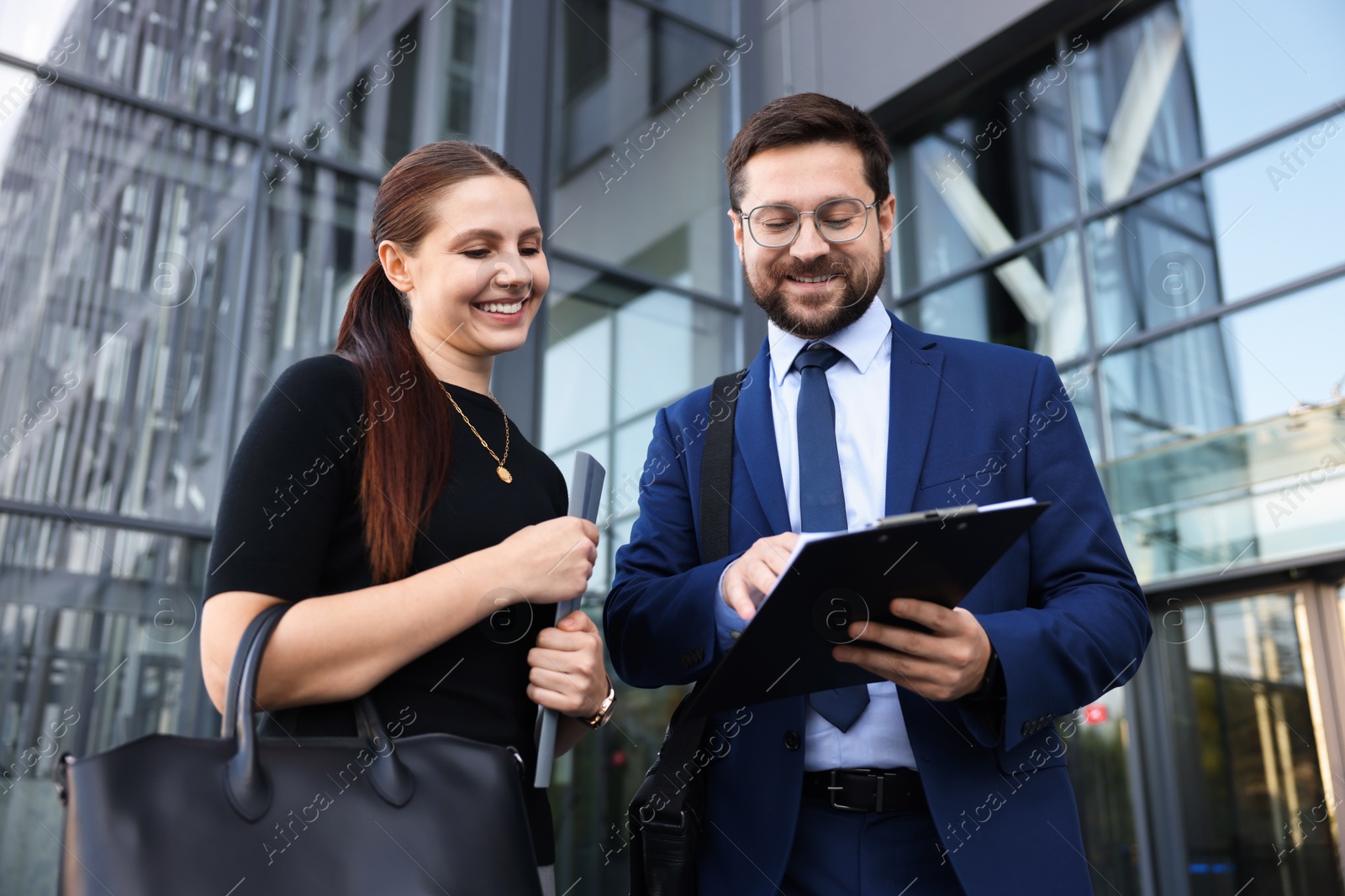 Photo of Happy coworkers discussing something near office building, low angle view