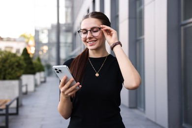 Photo of Successful businesswoman with smartphone near office building