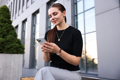 Photo of Successful businesswoman with smartphone near office building