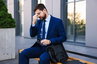 Photo of Tired businessman with glasses on bench outside office building