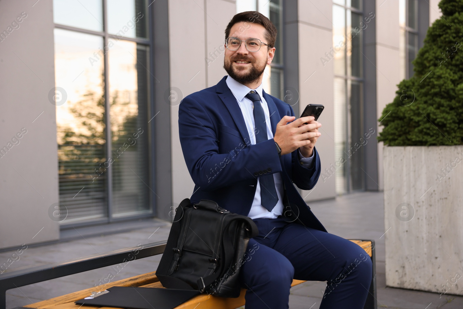 Photo of Successful businessman with smartphone near office building