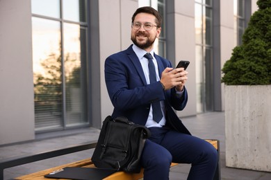Photo of Successful businessman with smartphone near office building