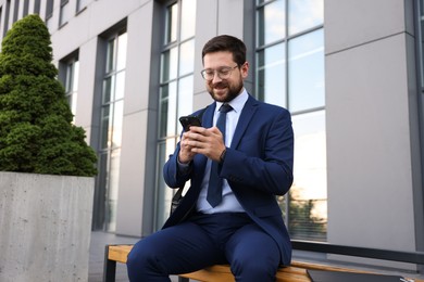 Photo of Successful businessman with smartphone near office building