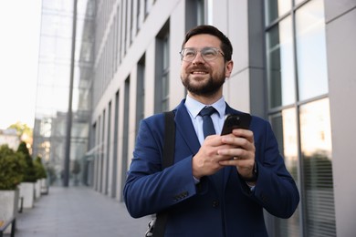 Photo of Successful businessman with smartphone near office building. Space for text