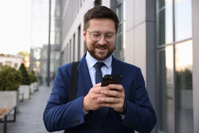 Photo of Successful businessman with smartphone near office building