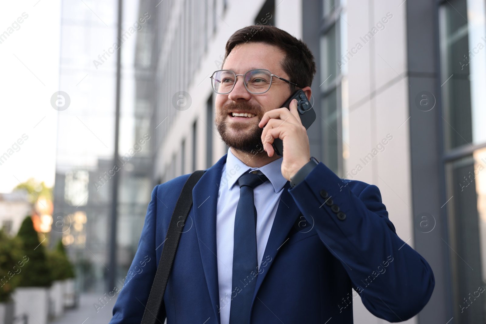 Photo of Successful businessman talking on phone near office building