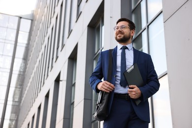Photo of Successful businessman with clipboard near office building, low angle view. Space for text
