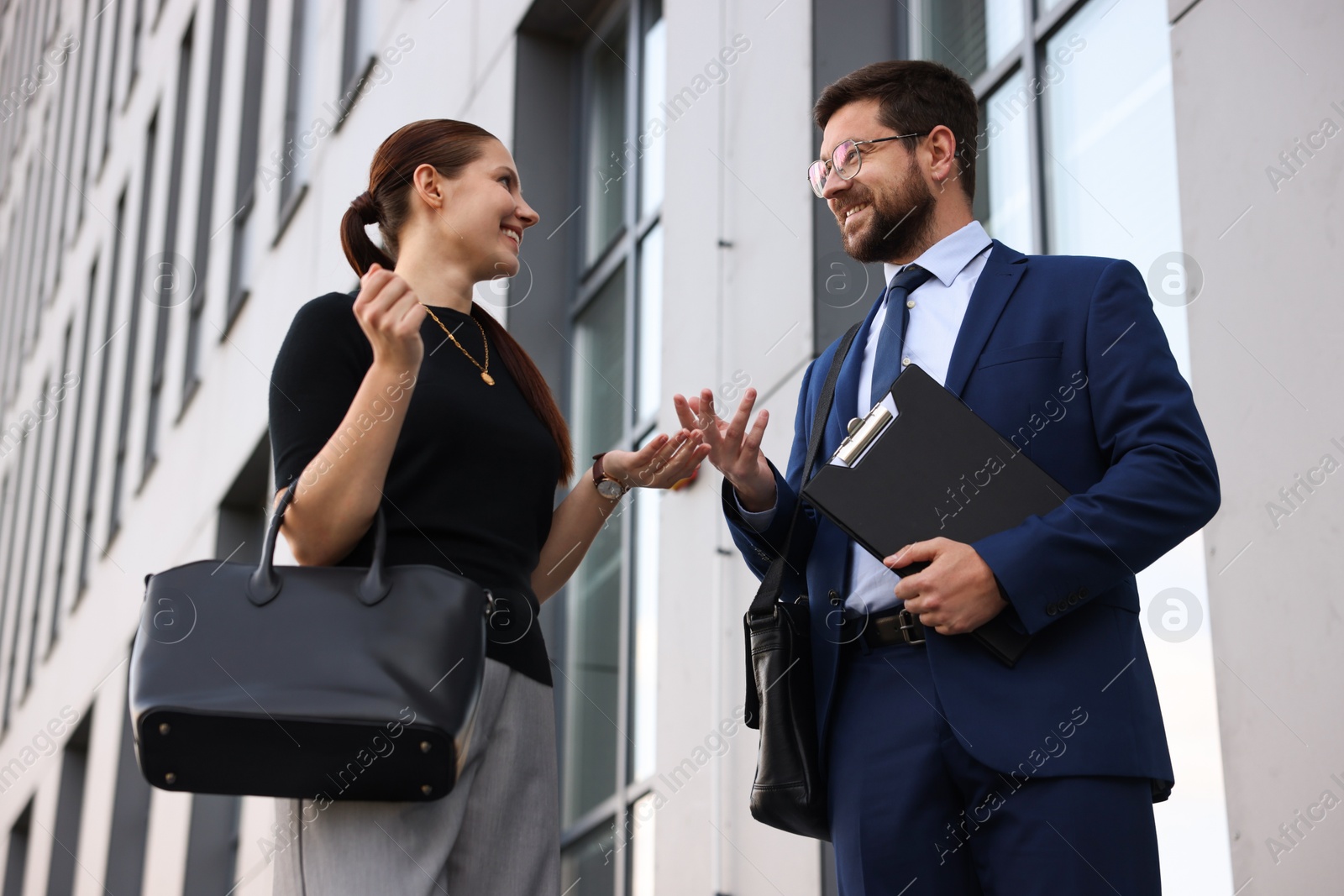Photo of Happy coworkers discussing something near office building, low angle view