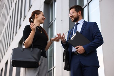 Photo of Happy coworkers discussing something near office building, low angle view